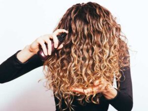 donna con capelli ricci che applica prodotto sulla chioma