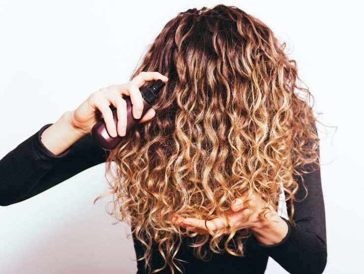 donna con capelli ricci che applica prodotto sulla chioma