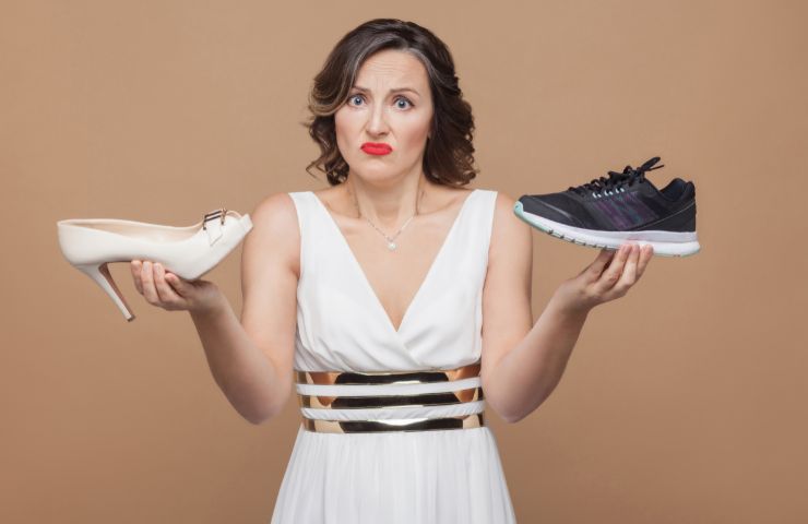 donna dubbiosa con in mano una scarpa con il tacco e un'altra sportiva